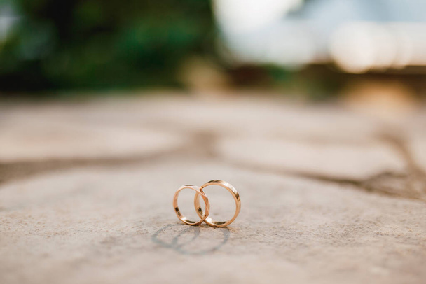 Arany gyűrűk egy esküvő függőleges helyzetben, homályos háttér. - Fotó, kép