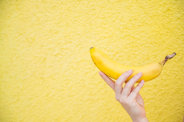 Close-up of a banana in a female hand on a yellow background. - Fotoğraf, Görsel