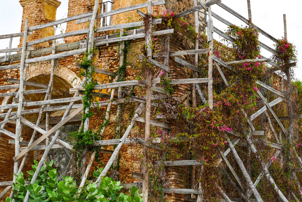 Casa siendo restaurada con varios postes de madera a su alrededor para que las paredes no caigan y las flores y plantas crezcan a su alrededor - Foto, imagen