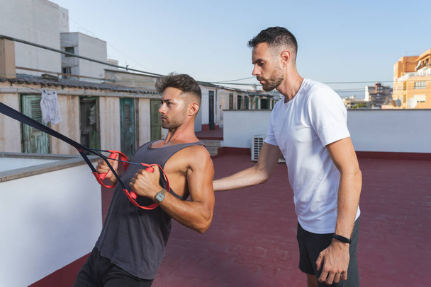 Atletyka człowiek robi ćwiczenia wiosłowania zawieszenie w sesji fitness z pomocą przyjaciela lub osobistego trenera - Zdjęcie, obraz