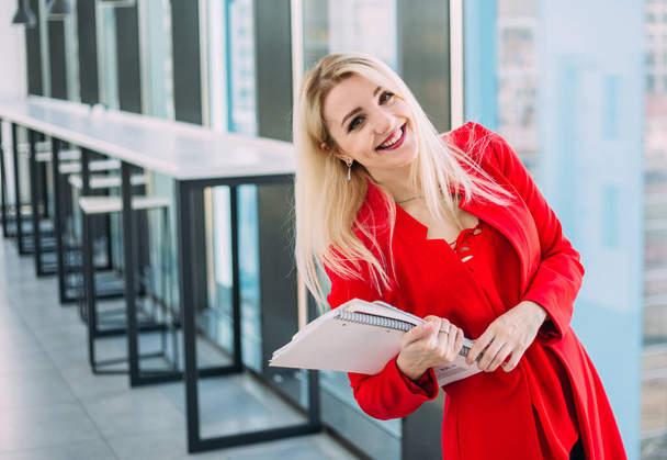 Attractive successful business lady in a red suit in a light office building by the window - Fotoğraf, Görsel