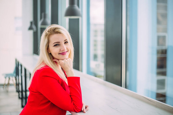 Attractive successful business lady in a red suit in a light office building by the window - Fotografie, Obrázek