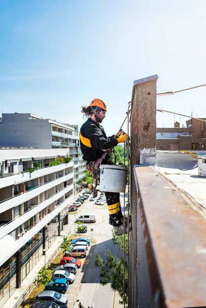 Mužský dělník visící na laně a výškovém stavebním projektu. Práce na izolaci stěn a fasádní malování dekorace práce. Tvrdé a nebezpečné pracovní prostředí - Fotografie, Obrázek