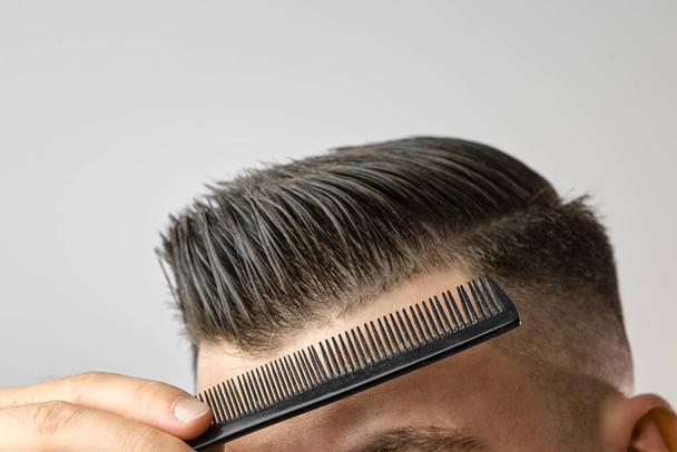 Крупним планом молодий чоловік розчісує волосся пластиковим гребенем. Укладання волосся після перукарні
.  - Фото, зображення