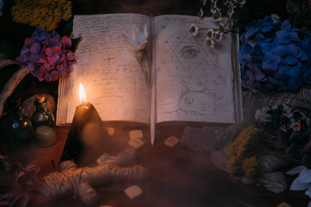Ouvre le vieux livre avec des sorts magiques, des runes, des bougies noires et des herbes sur la table des sorcières. Concept occulte, ésotérique, divination et wicca. Halloween vintage fond. - Photo, image