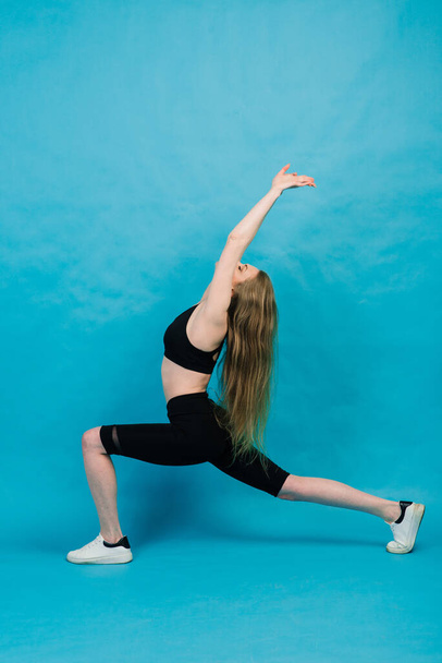 Γυμναστική. Γυναίκα με αθλητικά να τεντώνει πόδια, να ζεσταίνεται σε μπλε φόντο. - Φωτογραφία, εικόνα