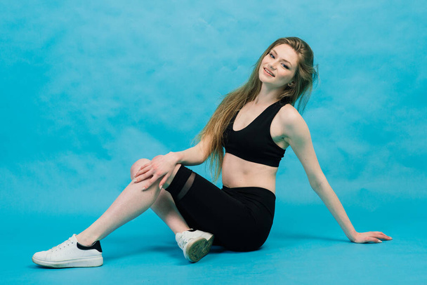 Fitness. Frau in Sportbekleidung streckt Beine, wärmt sich auf blauem Hintergrund auf. - Foto, Bild