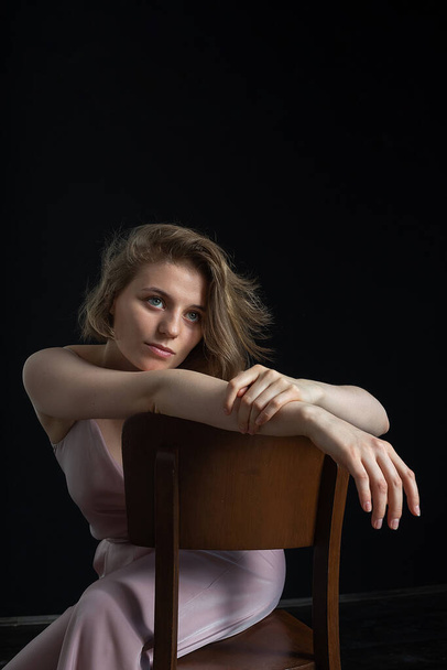woman with short hair posing in pink suit, sitting on chair on black background - Fotó, kép