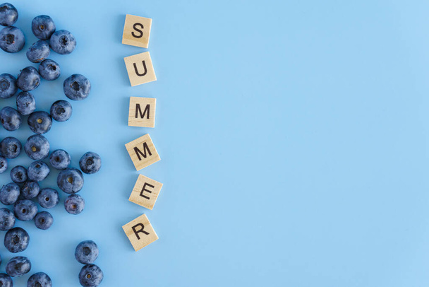 Healthy food, diet, gastronomy, fruits and berries, Harvesting, marketing, fitness concept - layout banner frame closeup of blueberries with inscription summer on plain blue background copy space - Foto, Bild