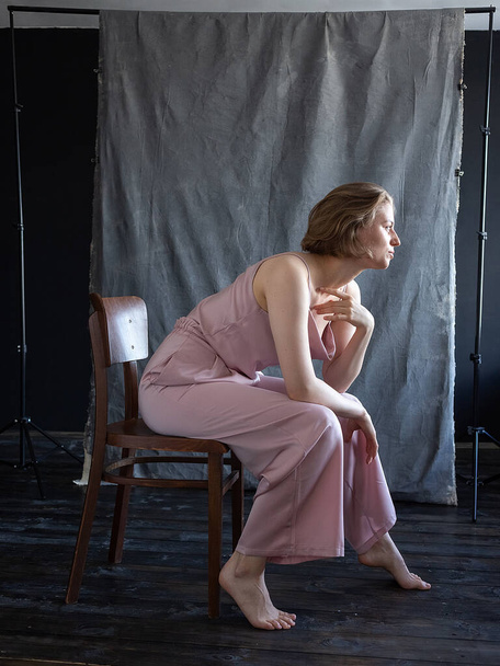 Kısa saçlı, pembe takım elbiseli, stüdyoda sandalyede oturan beyaz bir kadın. - Fotoğraf, Görsel