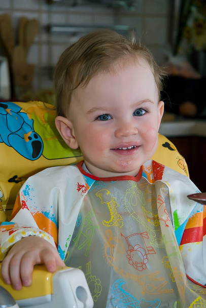 Un niño de un año comiendo sentado en una trona. Retrato de un bebé lindo y feliz, enfoque selectivo. - Foto, imagen