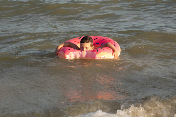 A 5-year-old boy bathes in a donut-shaped life ring on a sunny day - Photo, Image