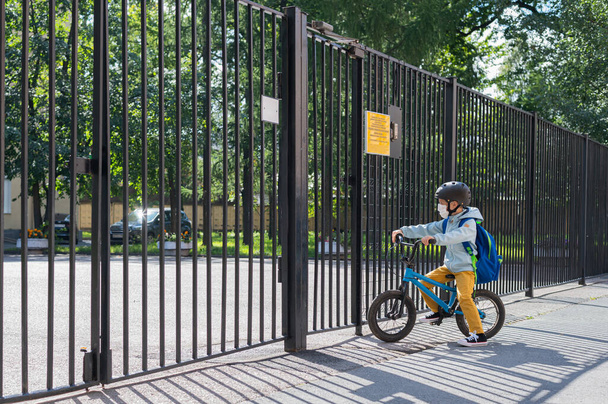 A masked boy stands at the school gate with a Bicycle. Back to school. New normal. - Fotografie, Obrázek