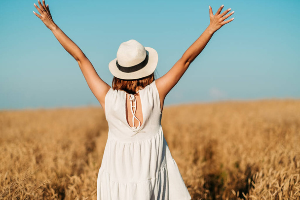 A woman, a girl is standing backwards in a wheat field, her hands raised to the sky. High quality photo - Fotografie, Obrázek