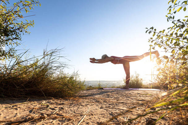 Woman yoga master doing at sunrise exercise in position warrior - Φωτογραφία, εικόνα