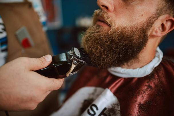 Close up of the hands of a barber trimming a young caucasian man's beard. New beard and hairstyle - Foto, imagen