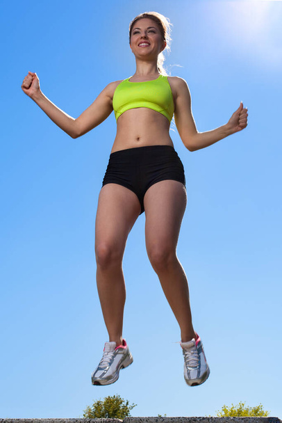 Full length portrait of caucasian young woman jumping in fitness wear outdoors  - Zdjęcie, obraz