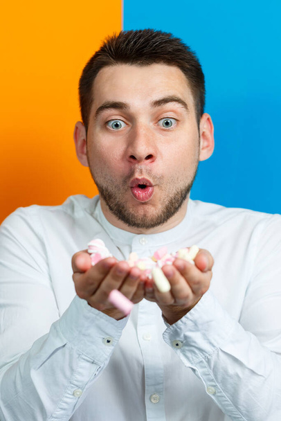 A man eats marshmallows from his hands. Bright man portrait. Sweets in the hands of a guy. Cheerful man portrait with sweets - Foto, Imagen