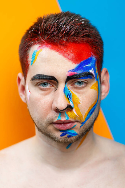 Makeup on the skin. Portrait of a young man with colored paint on a yellow background. Professional Makeup Fantasy Art Makeup - Photo, Image