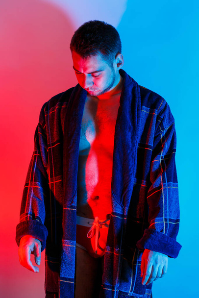 バスローブと下着を着た男。オスの体に赤と青のスタジオ照明。途方もない男モデル - 写真・画像