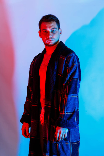 Een man in een badjas en ondergoed. Studio verlichting rood en blauw op een mannelijk lichaam. Schandalig mannelijk model - Foto, afbeelding