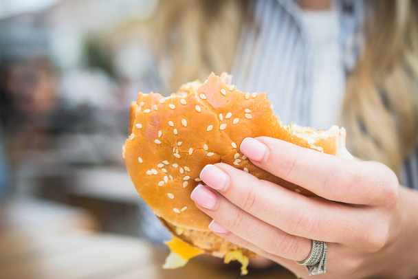 Tasty unhealthy burger sandwich in female hands close up - 写真・画像