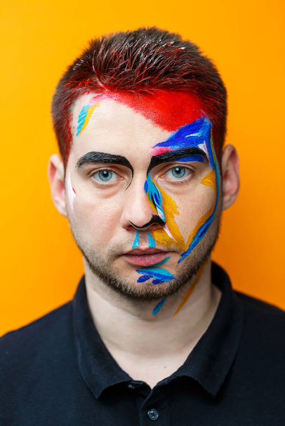 Makijaż na skórze. Portret młodego mężczyzny w kolorze farby na żółtym tle. Profesjonalny makijaż Fantasy Art makijaż - Zdjęcie, obraz