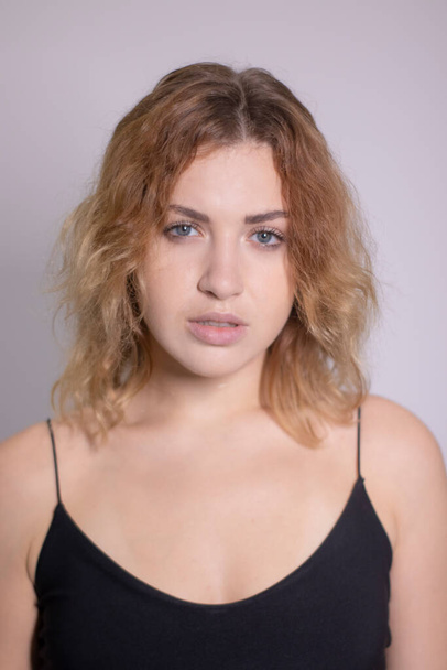 emotioneel portret van een mooie krullende blonde-roodharige in zwart ondershirt - Foto, afbeelding