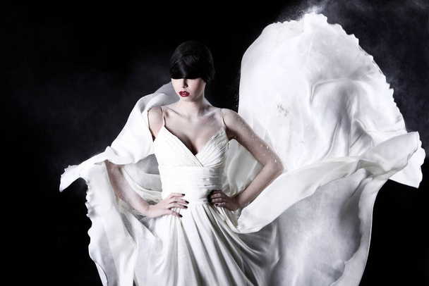 mooi meisje in witte jurk en vliegende stof op zwarte achtergrond - Foto, afbeelding