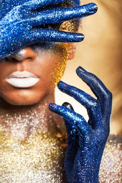Portrait of a woman who is posing covered with blue and gold paint - Foto, Bild