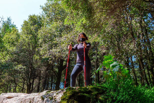 mujer caminando a través de un entorno natural con el bastón y su máscara - Foto, Imagen