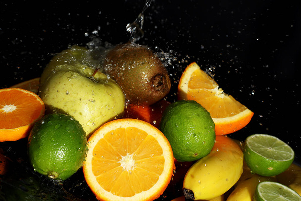 Νωπά φρούτα και νερό πιτσιλίζονται σε μαύρο φόντο - Φωτογραφία, εικόνα