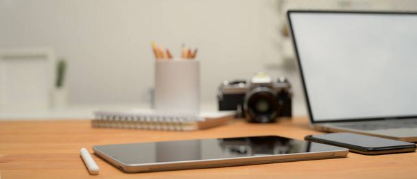木製の机の上にデジタルタブレット、ラップトップ、カメラ、スマートフォンや文房具でワークスペースのビューを閉じます。 - 写真・画像