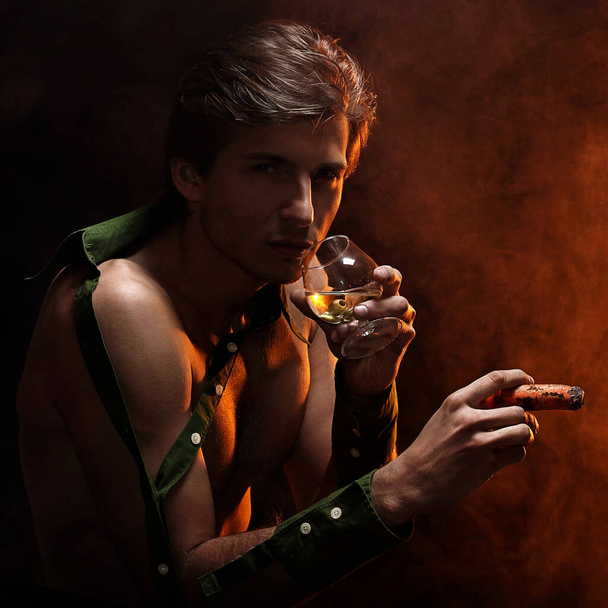 Artistic picture of handsome man with naked torso smoking cigar and drinking wine - Photo, image