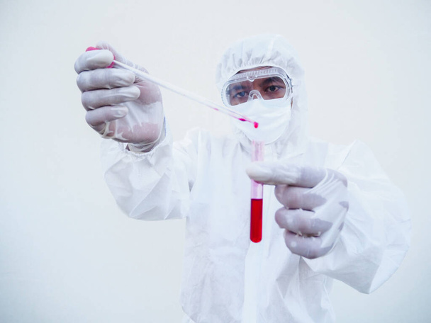 Азиатский врач или ученый в униформе СИЗ. Личный защитный костюм сбрасывает кровь в пробирку для анализа крови. коронавирус или COVID-19 концепция изолированного белого фона - Фото, изображение