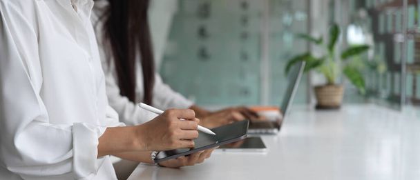 Seitenansicht weiblicher Hände, die digitale Geräte benutzen, während sie nebeneinander im Co-Working Space sitzen - Foto, Bild