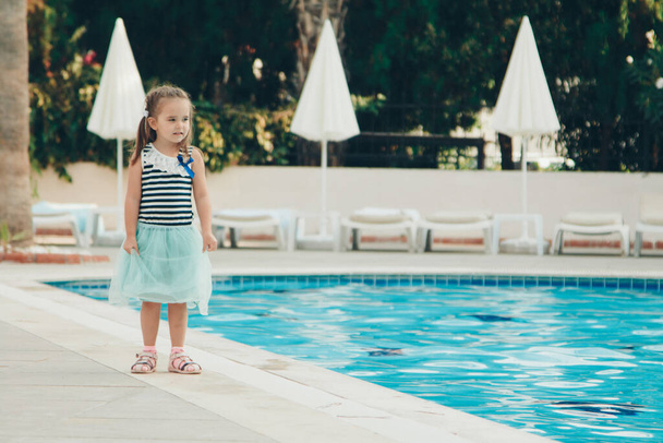 A little girl walks by the pool. Holidays in hot countries. the territory of the hotel - 写真・画像
