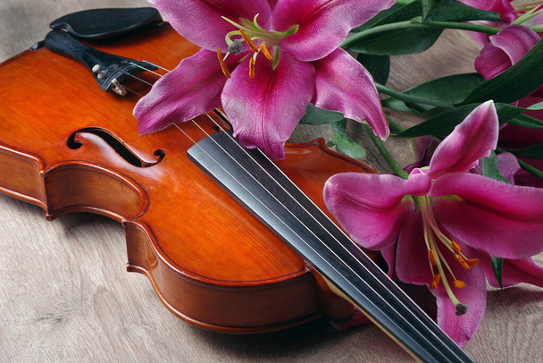 Geige und Lilienblüten auf einem hölzernen Hintergrund - Foto, Bild