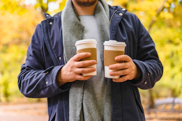 男は友人にコーヒーを持って屋外の秋の都市公園のライフスタイルに行く - 写真・画像