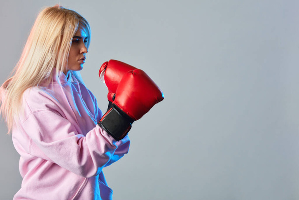 Sporty sexy woman wearing pink hoodie and red boxing gloves on white background - Photo, Image