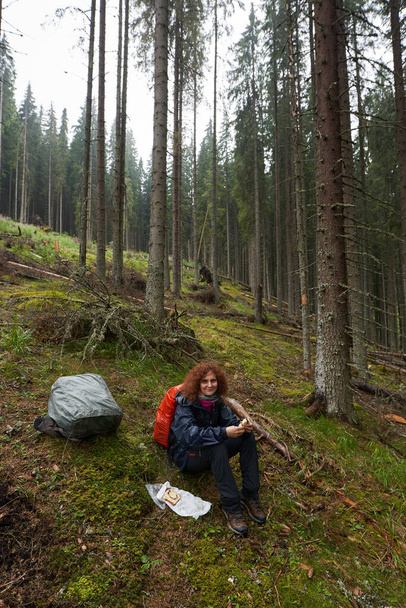 Woman tourist with raincoat and backpack hiking through mountain pine forest in a rainy day - Fotografie, Obrázek