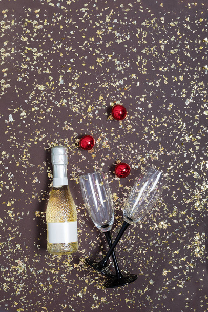 Neujahrshintergrund mit Sektflasche, Gläsern und Weihnachtsdekoration auf dunklem Hintergrund mit Konfetti von oben. Neujahr, Weihnachtsgrußkarte. Vertikale Orientierung. - Foto, Bild