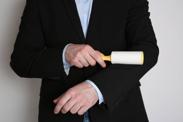 Man cleaning black jacket with lint roller on light grey background, closeup - Foto, afbeelding