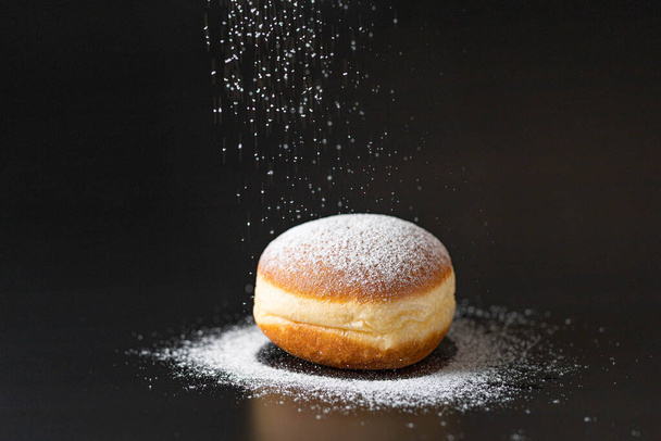 пончик з цукровою пудрою на чорному фоні
 - Фото, зображення