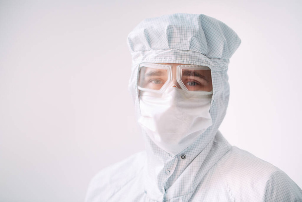 Portrait of a male doctor of European appearance in a medical mask, protective glasses and chemical suit. - Foto, afbeelding