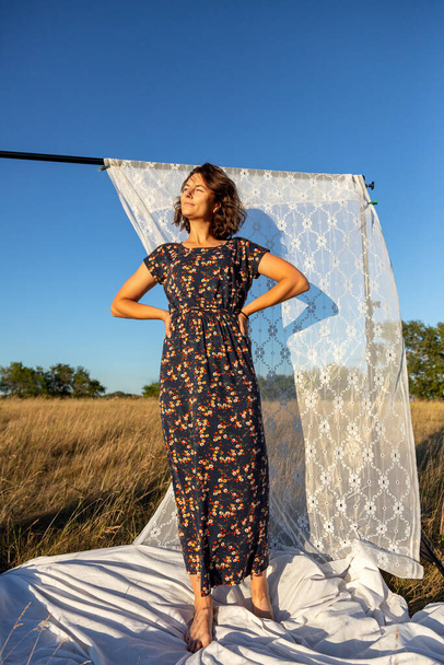 Pretty fresh  young woman  posing outdoors in field  and wearing in dress in the background a rack with white curtains .Concept of summer  holidays at village  and live style - Photo, Image