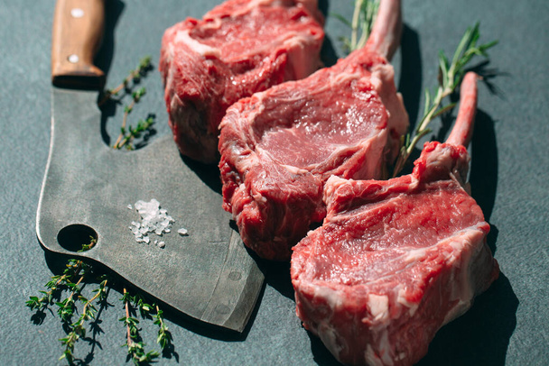 Raw steak with a meat cleaver on a dark stone background. - Фото, зображення