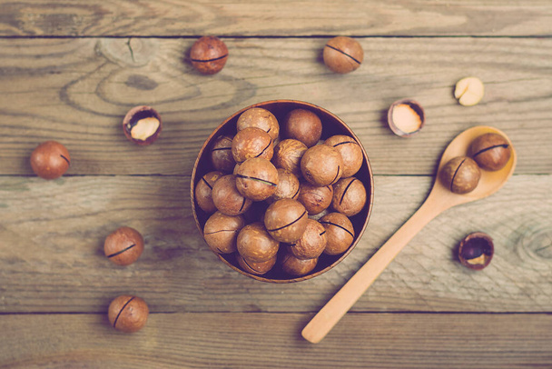 natural organic macadamia nuts in bowl on wooden table Flat lay Top view Healthy snack Nuts contain essential oil rich in vitamins B and PP, lot of fats and high in calories. Superfood - Photo, image