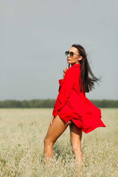 A young beautiful girl with a good figure, standing among a spacious field, she is wearing one red dress, autumn colors are all around! - Photo, image