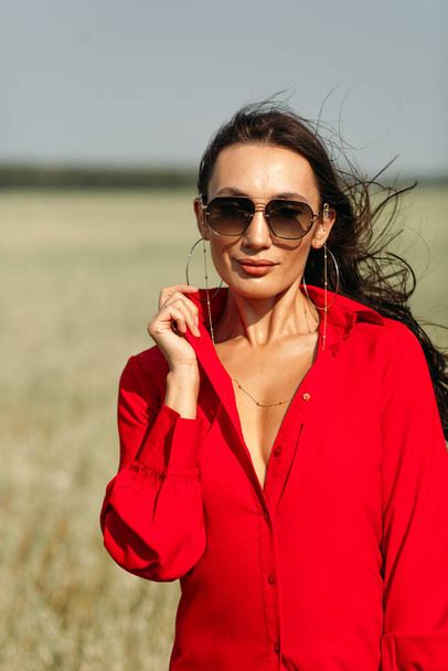 A young beautiful girl with a good figure, standing among a spacious field, she is wearing one red dress, autumn colors are all around! - Фото, изображение